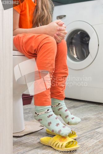 Image of Little girl is sitting on the toilet in the bathroom