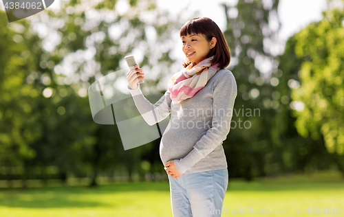 Image of happy pregnant asian woman taking selfie at park