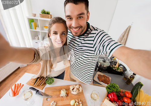 Image of couple cooking food and taking selfie at kitchen