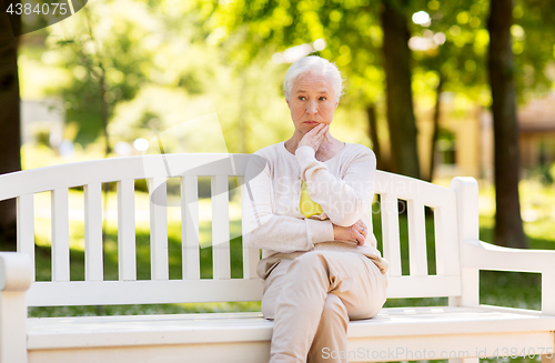 Image of sad senior woman sitting on bench at summer park