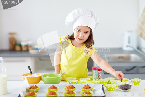 Image of little girl in chefs toque baking muffins at home