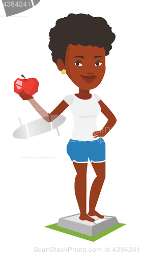 Image of Woman standing on scale and holding apple in hand.