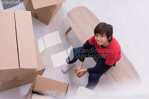 Image of boy sitting on the table with cardboard boxes around him top vie