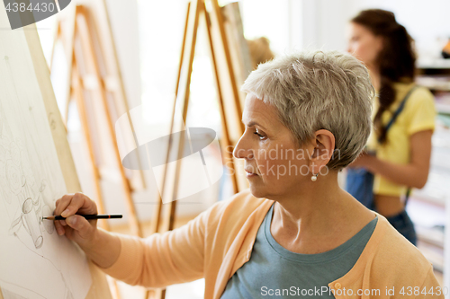 Image of senior woman drawing on easel at art school studio