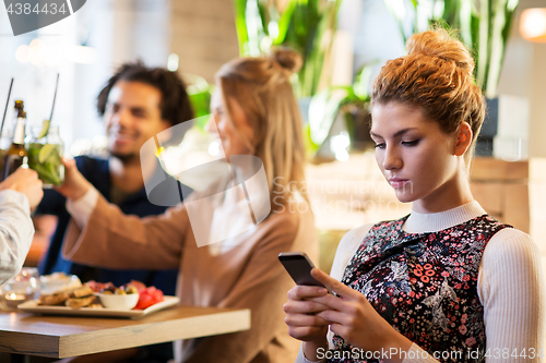 Image of woman with smartphone and friends at restaurant