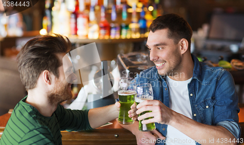 Image of male friends drinking green beer at bar or pub