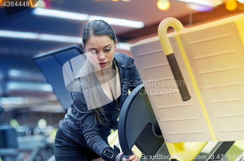 Image of young woman adjusting leg press machine in gym