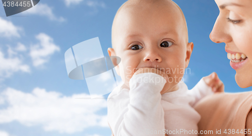 Image of happy mother with baby sucking fingers over sky