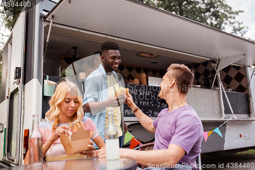 Image of happy friends with drinks eating at food truck