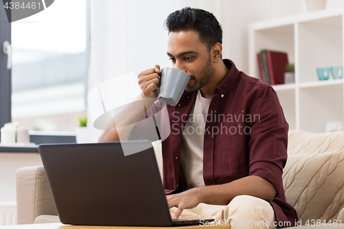 Image of smiling man with laptop drinking coffee at home