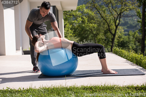 Image of woman and personal trainer doing exercise with pilates ball