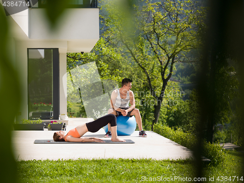 Image of woman and personal trainer doing exercise with pilates ball