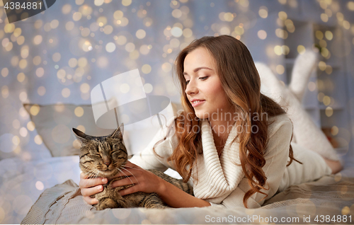 Image of happy young woman with cat lying in bed at home