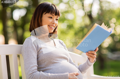 Image of happy pregnant asian woman reading book at park