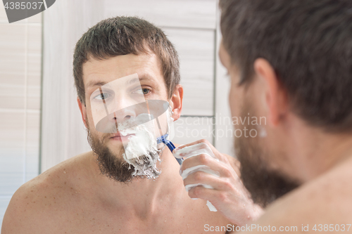 Image of A man shaves his beard very strong