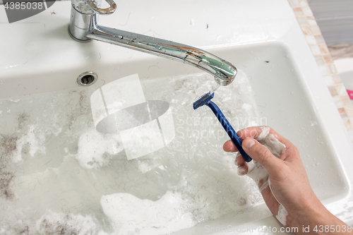 Image of The man\'s hand washes the shaver under the stream of water