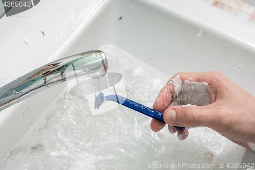 Image of The man\'s hand washes the shaver under the stream of water, close-up on top