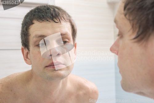 Image of A clean-shaven young man looks in the mirror