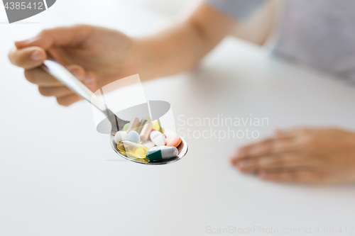 Image of close up of female hand holding spoon with pills