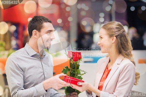 Image of happy couple with present and flowers in mall