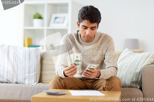 Image of man with calculator counting money at home