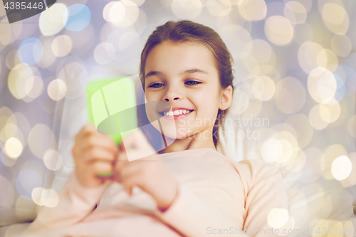 Image of happy girl in bed with smartphone over lights