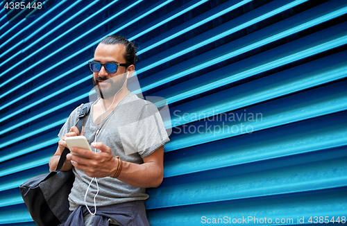 Image of man with earphones and smartphone over wall