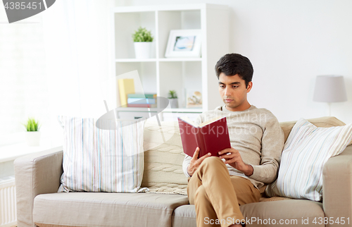 Image of man sitting on sofa and reading book at home