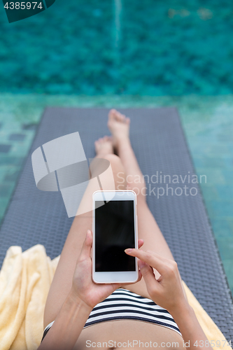 Image of Woman relax on sunbath in swimming pool with using mobile phone