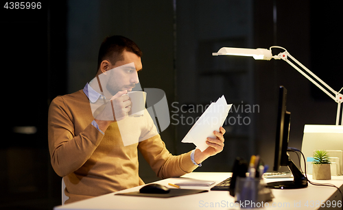 Image of man with papers and coffee working at night office