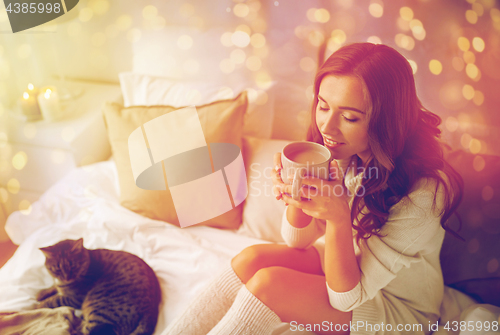 Image of happy woman with cup of coffee in bed at home