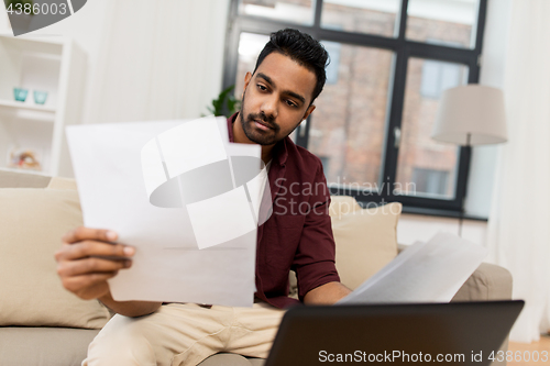 Image of upset man with laptop and papers at home