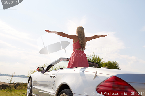 Image of happy young woman in convertible car at seaside