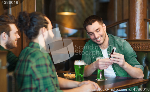 Image of friends with smartphone drinking green beer at pub