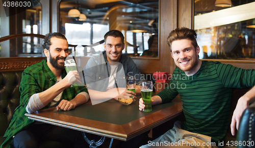 Image of male friends drinking green beer at bar or pub