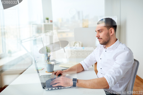 Image of happy businessman typing on laptop at office