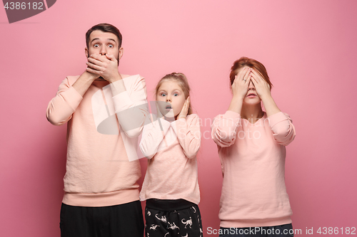 Image of Surprised young family looking at camera on pink