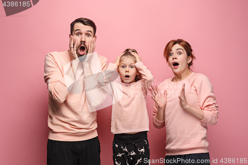 Image of Surprised young family looking at camera on pink