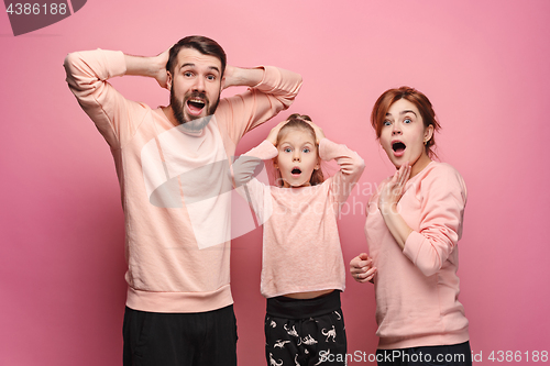 Image of Surprised young family looking at camera on pink