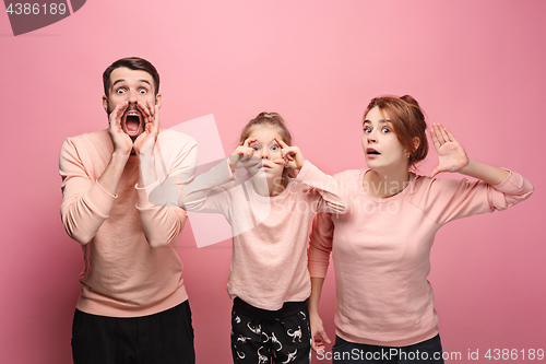 Image of Surprised young family looking at camera on pink