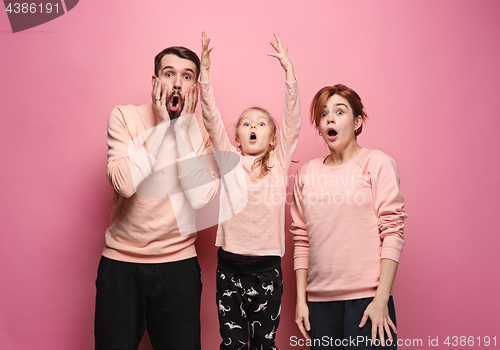 Image of Surprised young family looking at camera on pink
