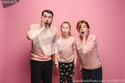 Image of Surprised young family looking at camera on pink