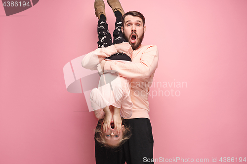 Image of cheerful father playing with daughter on pink