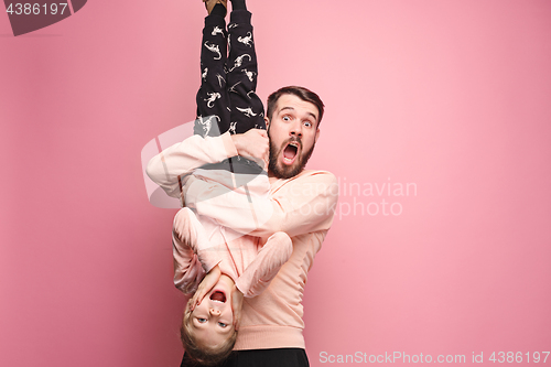 Image of cheerful father playing with daughter on pink