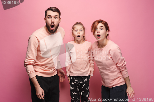 Image of Surprised young family looking at camera on pink