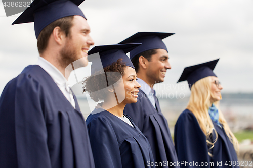 Image of happy students or bachelors in mortar boards