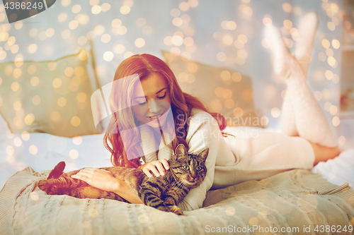 Image of happy young woman with cat lying in bed at home