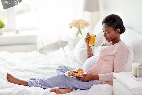 Image of pregnant woman with orange juice and pastry in bed