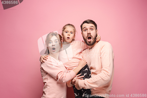 Image of Surprised young family looking at camera on pink