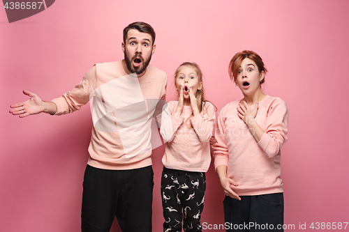 Image of Surprised young family looking at camera on pink